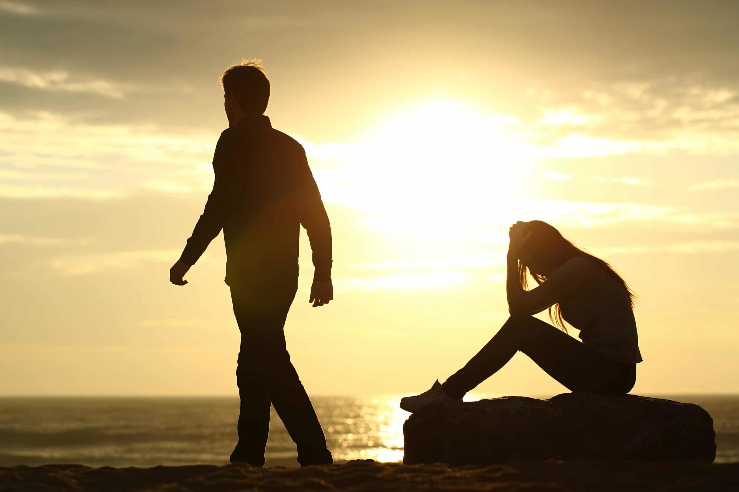Man walking away from distraught woman on the beach in the sunset.