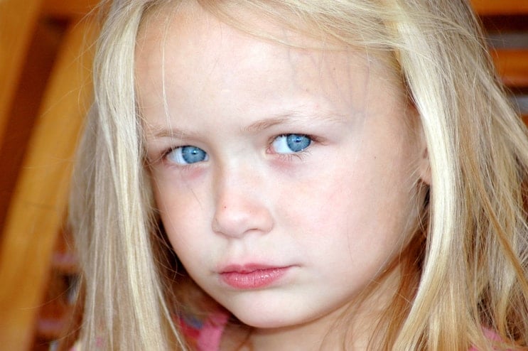 Sad liitle girl with blonde hair and blue eyes looking into the camera.