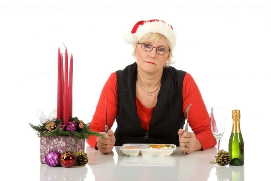 Despondent woman in Santa hat eating a TV Dinner alone.