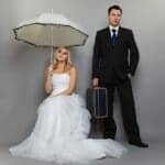 Disgusted bride holding an umbrella while her disengaged groom holds a suitcase