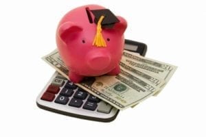 Piggy bank with a graduation cap sitting atop a calculator and money.