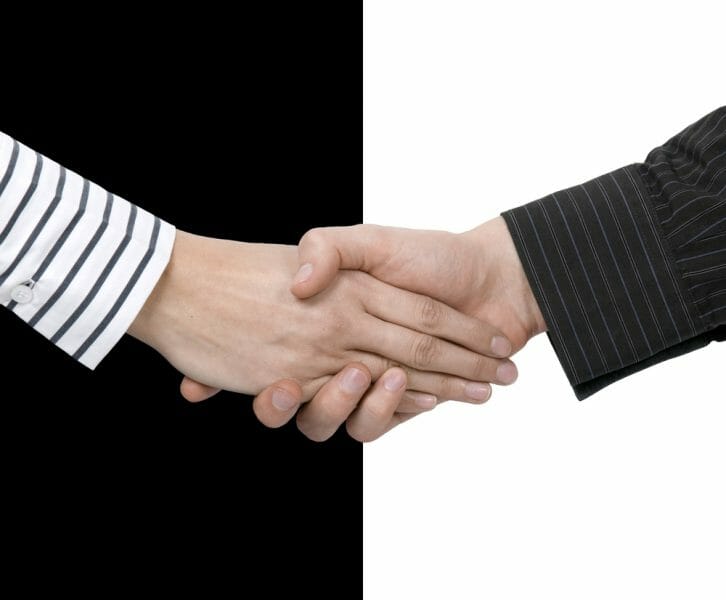 Man and woman's hands in a handshake in front of a black and white background.