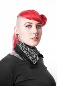 Woman with half-shaved head, pink hair, big ear loops, a nose ring and piercings.