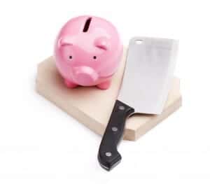 Piggy bank on a cutting board next to a meat cleaver.