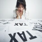 Terrified woman staring at a desk full of papers that say "Tax" in big bold letters