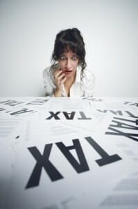 Scared woman looking at papers on a desk that say "Tax" in big letters.