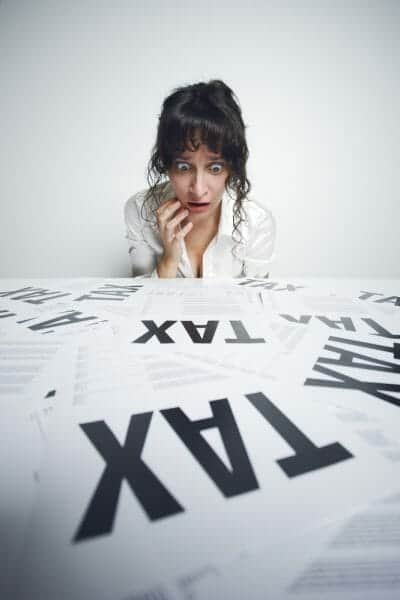 Scared woman looking at papers on a desk that say "Tax" in big letters.