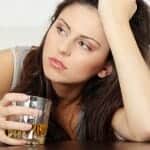 Upset woman holding her head and a glass of whiskey
