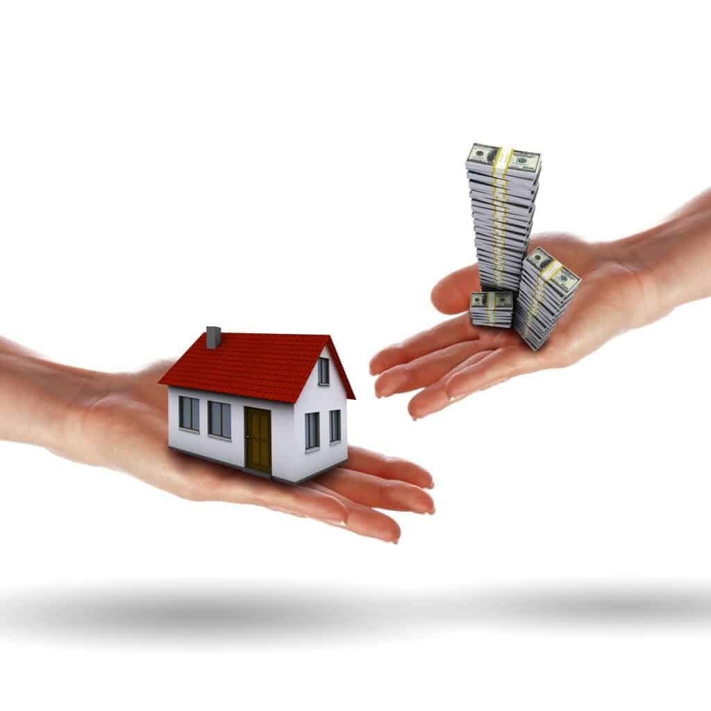 Close up of one hand holding a house and another holding a large stack of money.