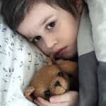 Sad boy in bed with a teddy bear