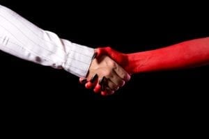 Close up of a business man's hand shaking with the devil's hand.