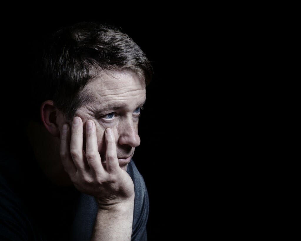Closeup side view of mature man with his chin in hand displaying depression on black background