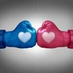 Blue and pink boxing gloves with hearts on them facing off.