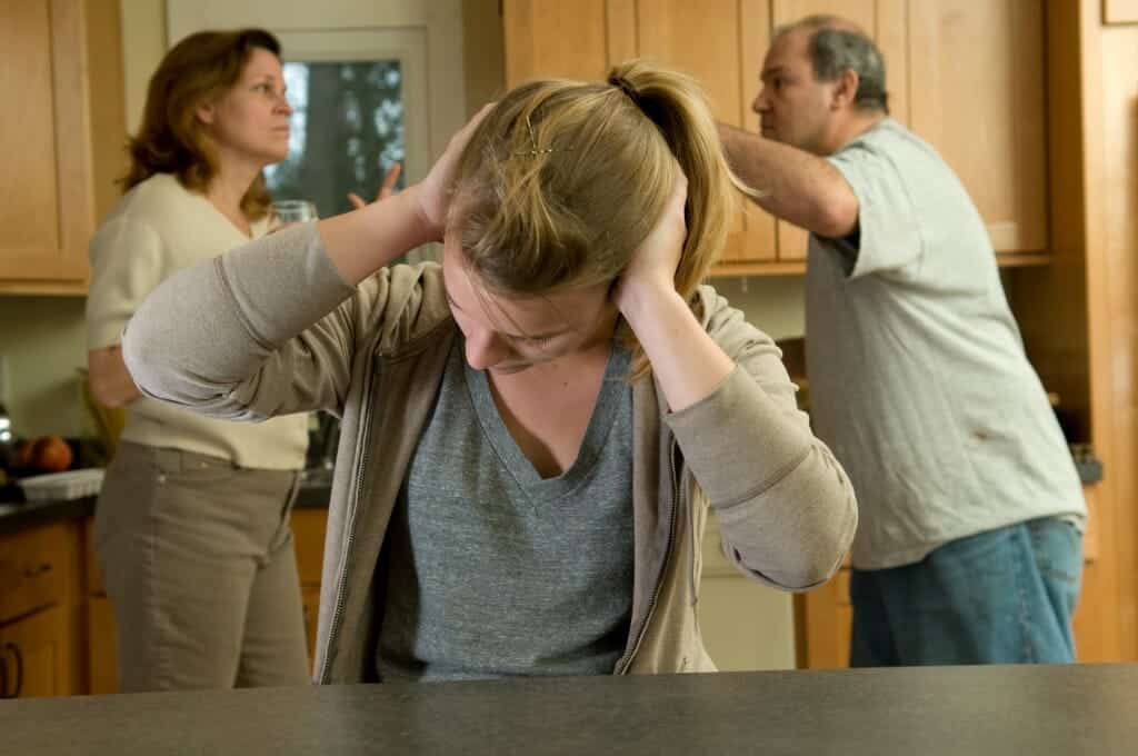 Young girl covering her ears as her parents argue in the background.