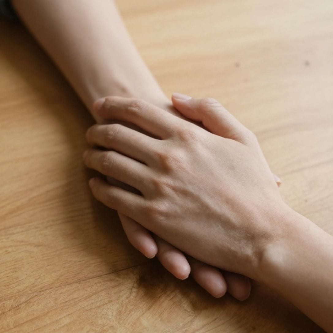 AI image of two hands clasped together on a wooden table, one hand is clearly comforting the other, a gesture of support and kindness