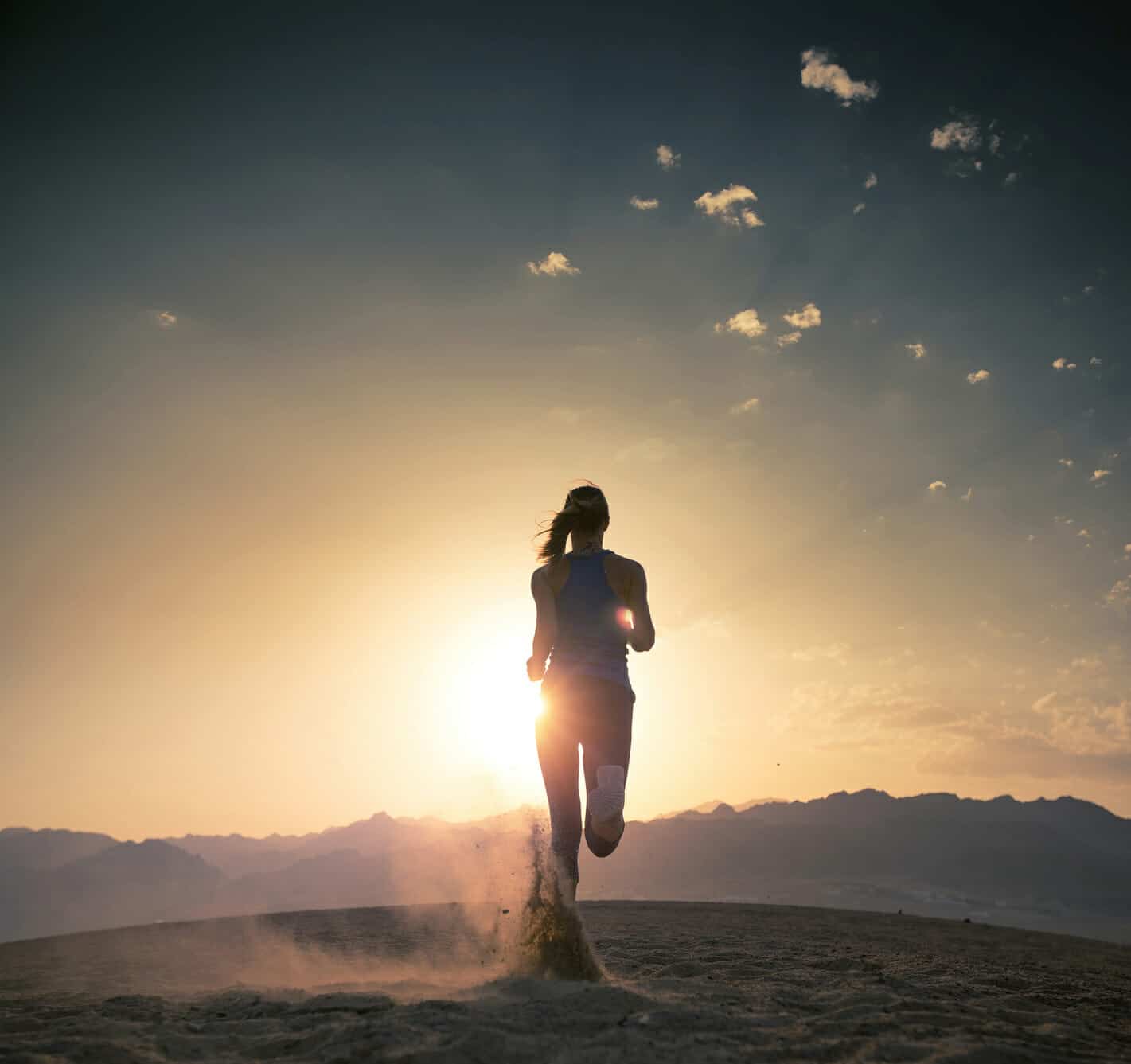 Young female athlete running in the desert at sunset