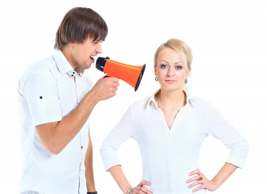 Man with megaphone talking into disgusted woman's ear.
