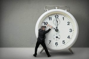 Man tugging at the hands of a giant alarm clock. Make time go backwards.