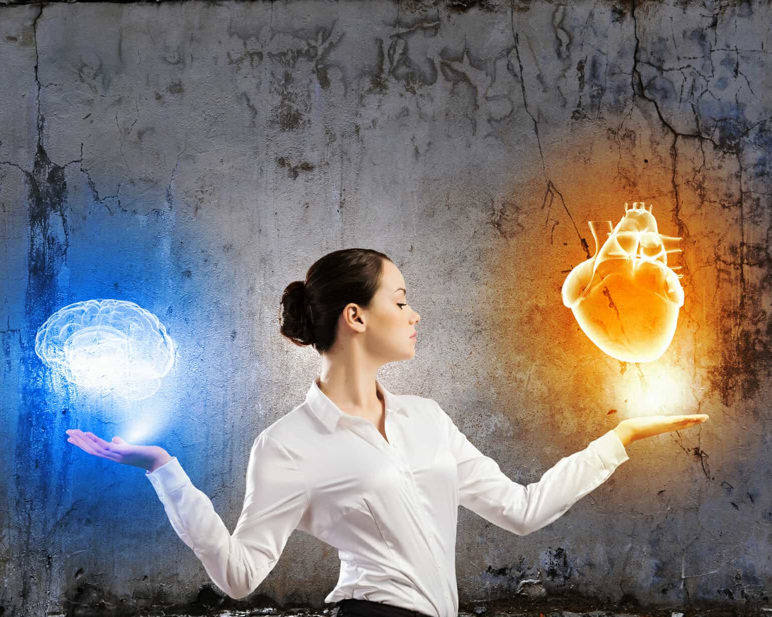 Serious young business woman holding holographic illustrations of a brain in one hand and a heart in the other.