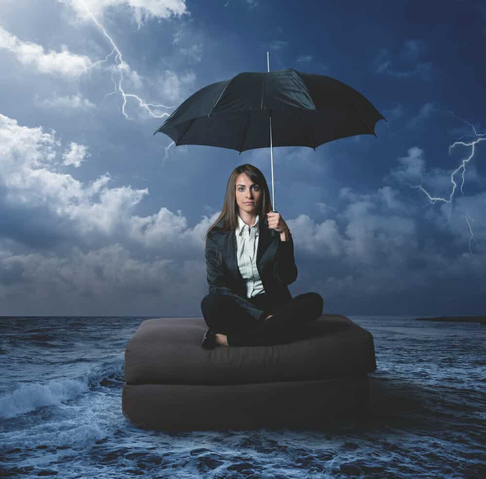 Woman on a storm floating on a cushion in the ocean with an umbrella over her head.