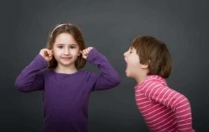 Small boy screaming at young girl with her ears plugged.