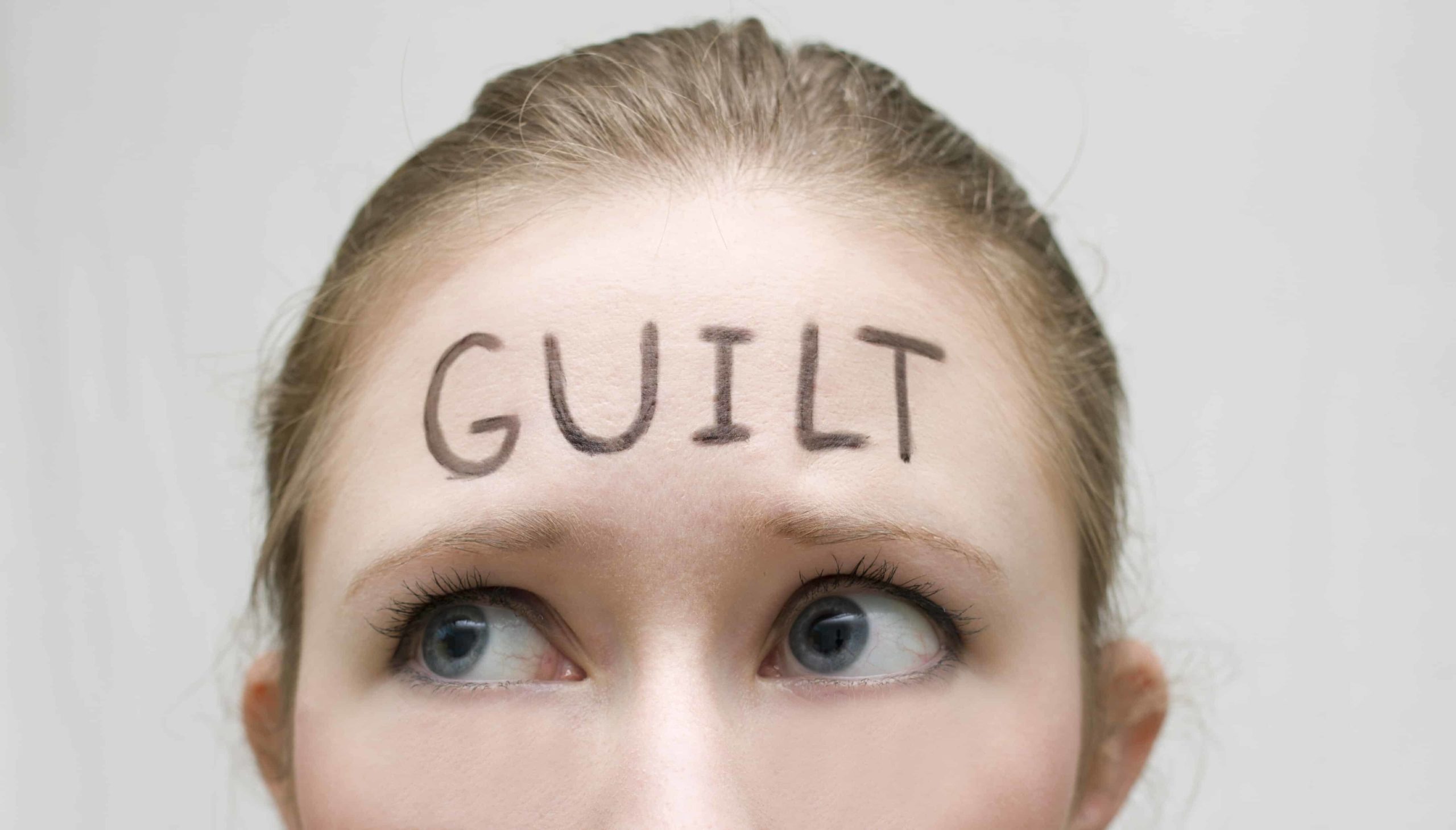 Close up of a nervous woman with the word "Guilt" written on her forehead.