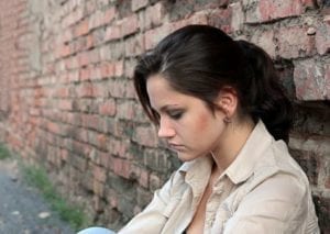 Sad woman sitting against a brick wall.