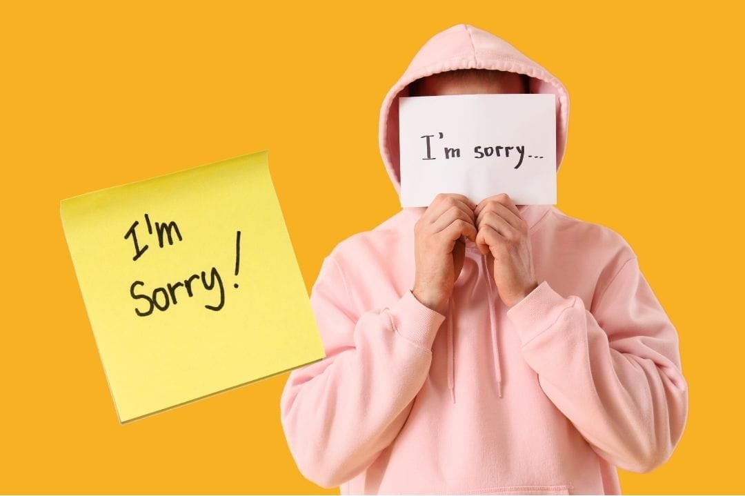 man holding up I'm sorry sign man holding up I'm sorry sign covering his face