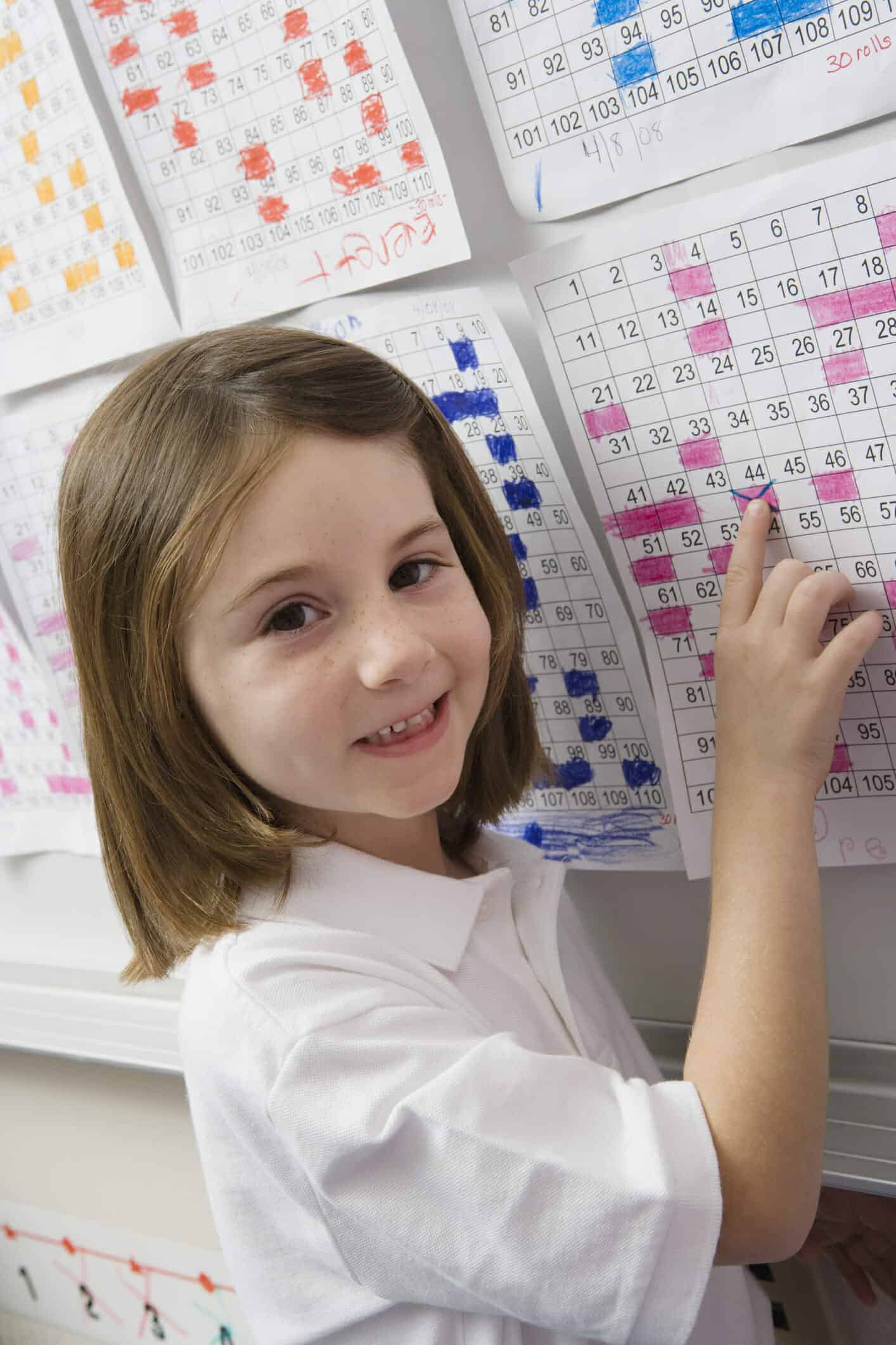 Smiling young girl pointing to a colored calendar page on the wall.