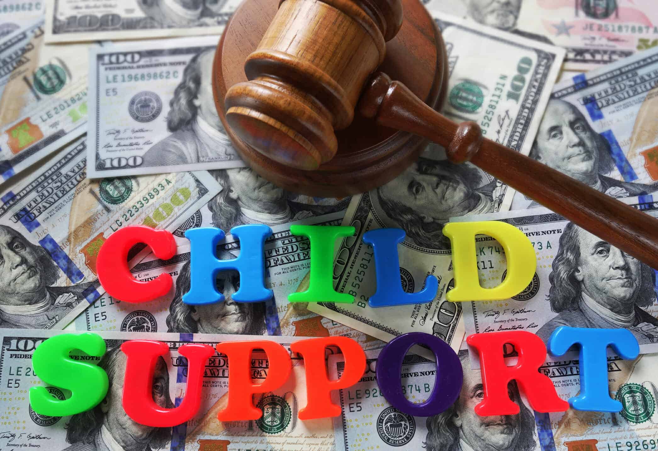 Multi-colored plastic children's letters spelling "child support" on top of a pile of $100 bills with a judge's gavel.