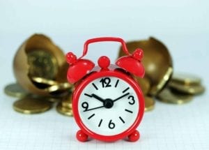 Red alarm clock with gold coins in the background