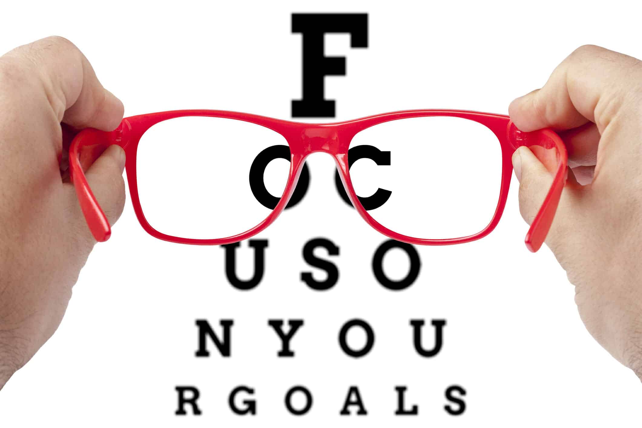 Hand holding red glasses. Behind is an eye chart with letters spelling: FOCUS ON YOUR GOALS.