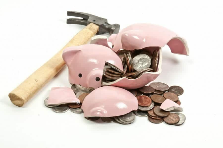 Broken piggy bank filled with coins and a hammer next to it.
