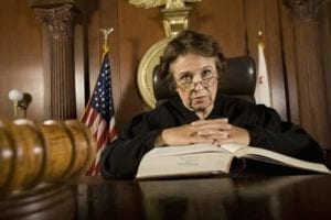 Stern looking older judge looking down from the bench with a law book in front of her.