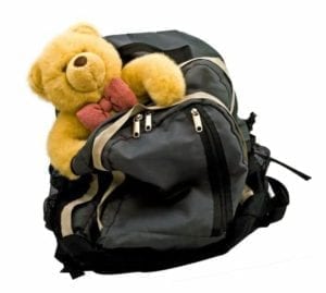Yellow teddy bear hanging out of backpack.