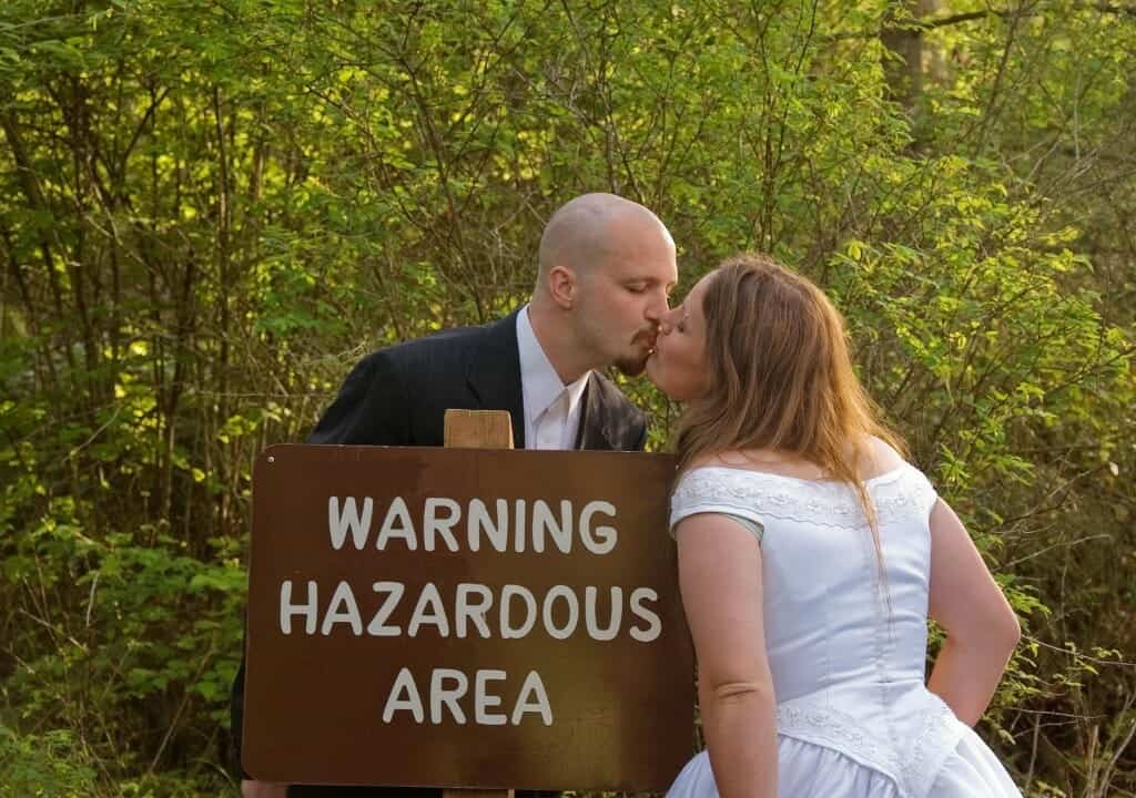 Bride and groom kissing next to a sign that says, "Warning Hazardous Area"
