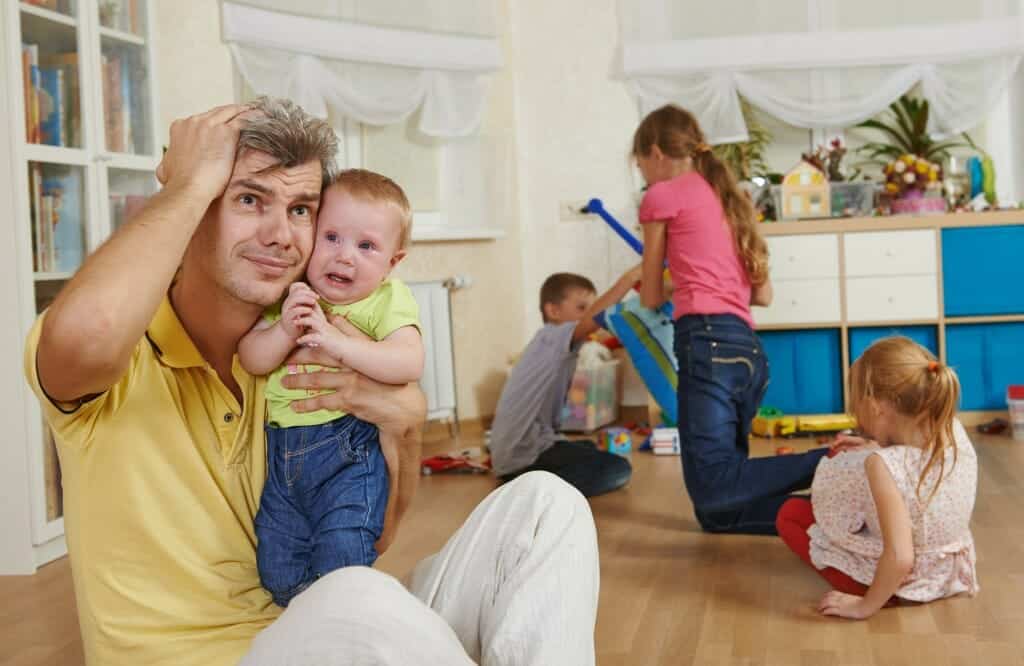 Parenting after divorce: Overwhelmed father sits among children playing