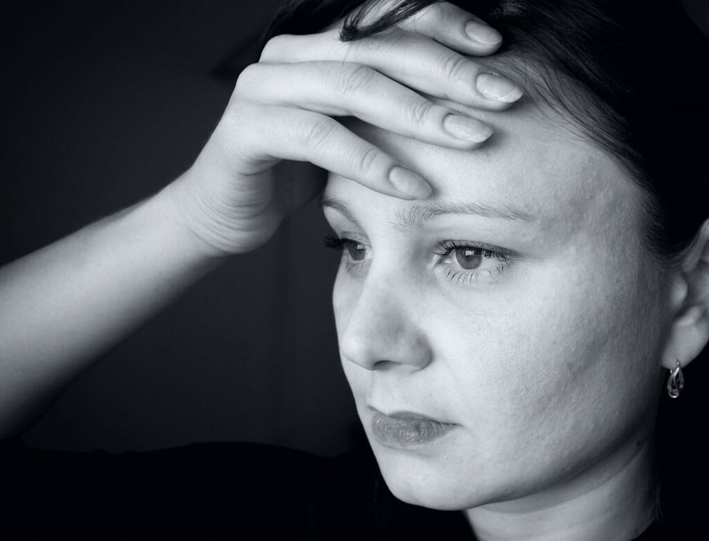 Black and white picture of a depressed woman holding her head.