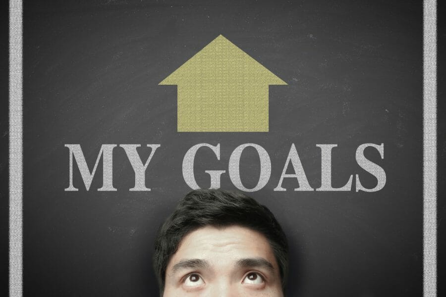 Head of a man standing in front of a blackboard with the words "My Goals" and an arrow pointing up on top of his head.