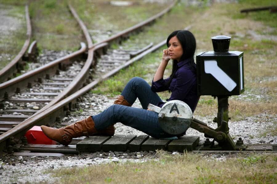 Young woman sitting next to intersection of train tracks.