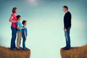 Wife and children stand on one side of a cliff and the husband stands on the other.