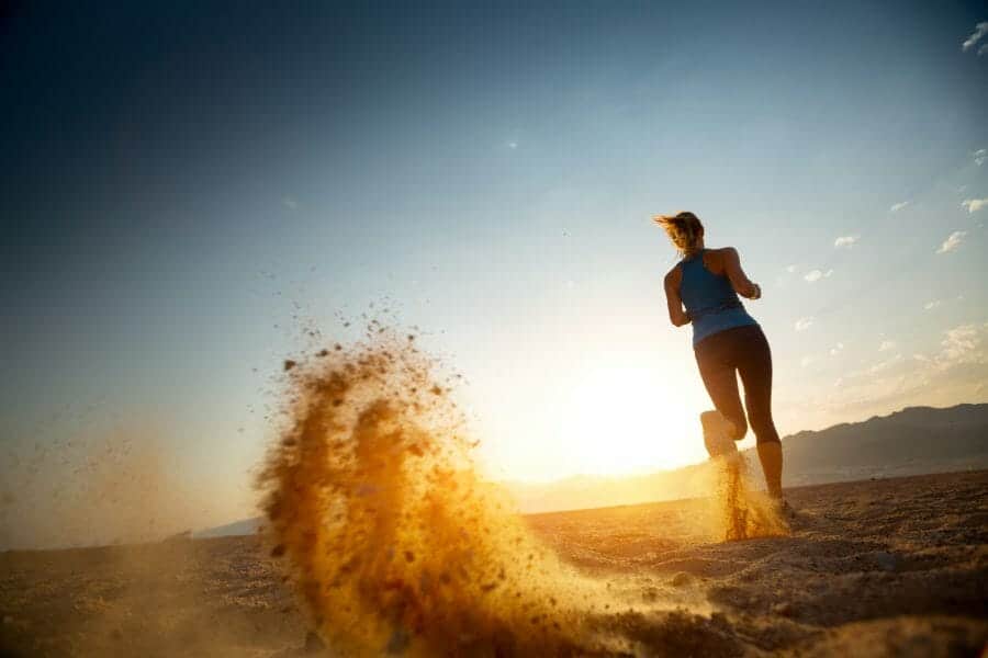 Woman kicking up dirt, running in the sunrise in the desert