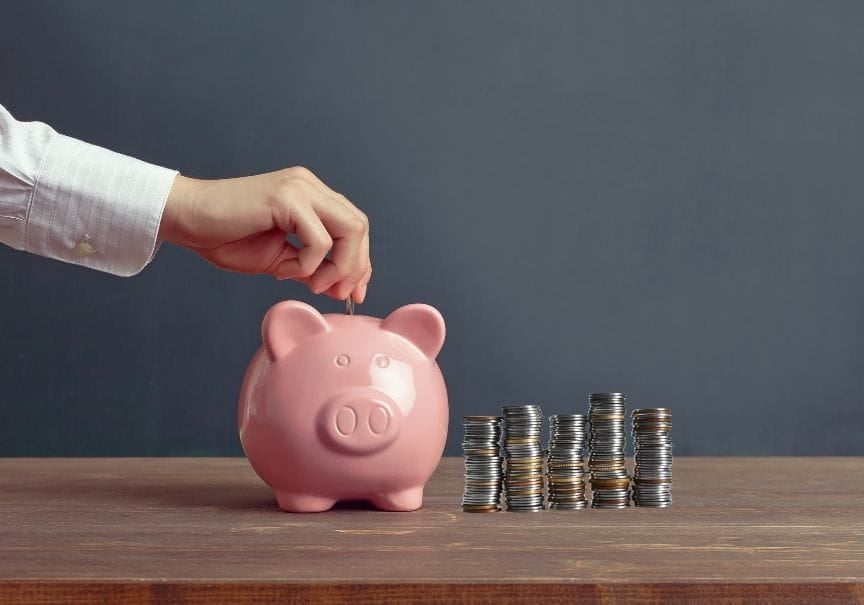 piggy bank with pile of coine piggy bank on a table with a pile of coins next to it