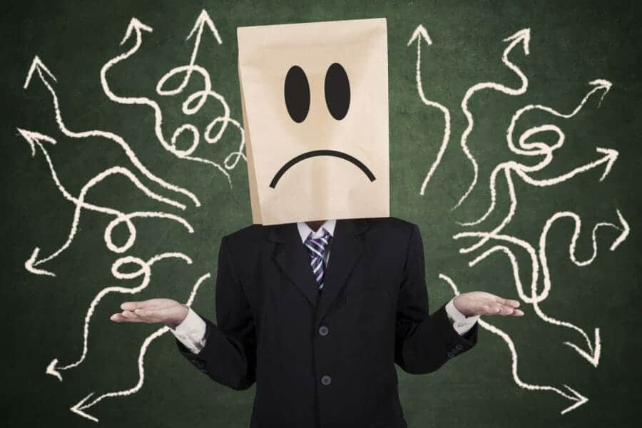 Person with bag over head and a confused face standing in front of a chalkboard with arrows on it pointing every which way.