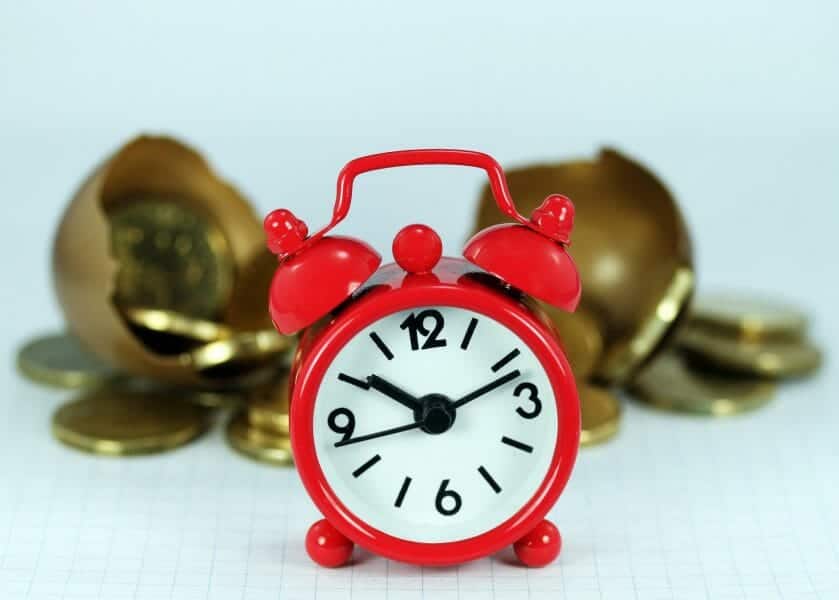 Red alarm clock in front of gold coins: save time and money