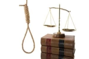 Noose hanging next to a stack of law books with the scales of justice on top.