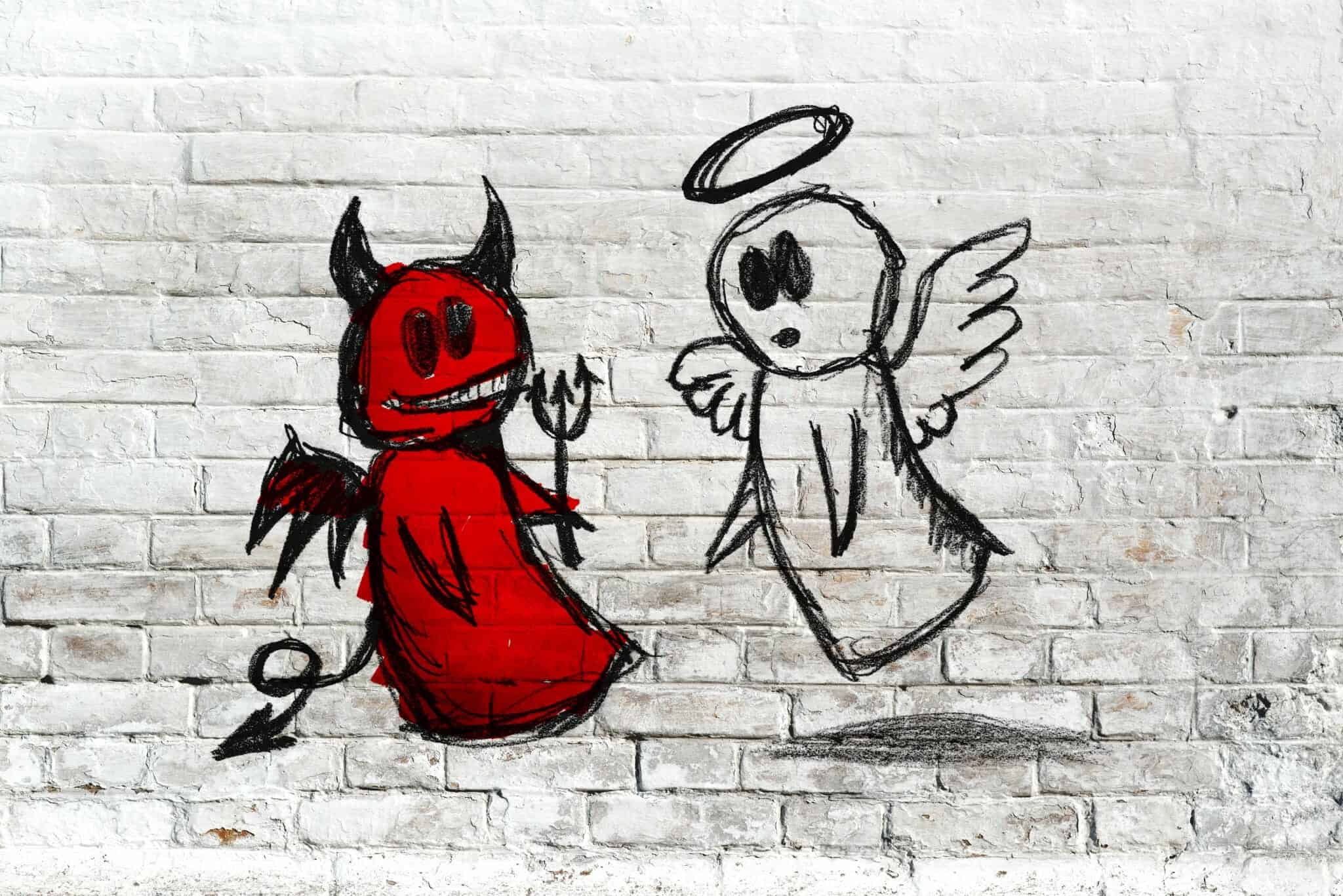 White angel and red devil drawn on a brick wall.