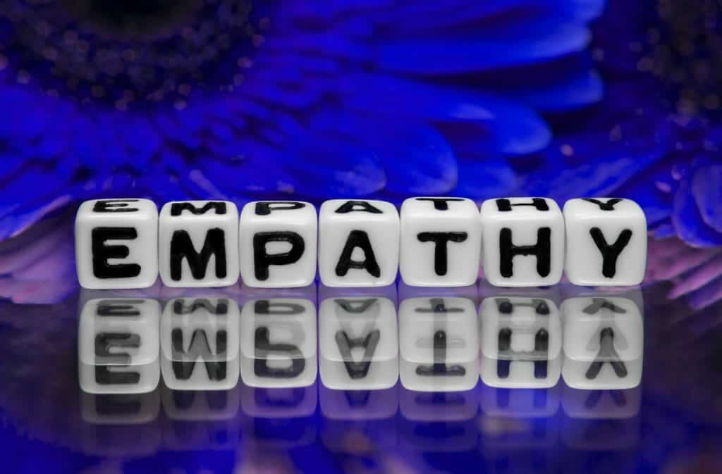 Empathy spelled out on dice with blue flowers in the background.