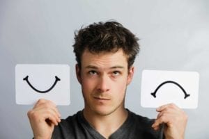 Man trying to decide to divorce holding a card with a smile and a card with a frown.