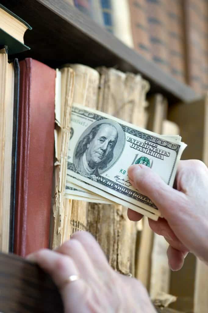 Close up of hand putting $100s in a shelf of books, hiding money